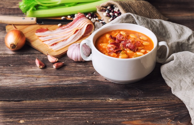 Zuppa di fagioli fatta in casa in una ciotola bianca sul tavolo in legno rustico con ingredienti.