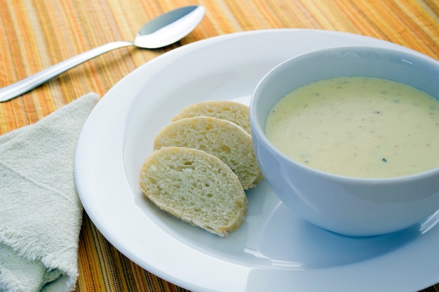 Zuppa di formaggio su una ciotola bianca con pane a fette e un cucchiaio su sfondo arancione a strisce