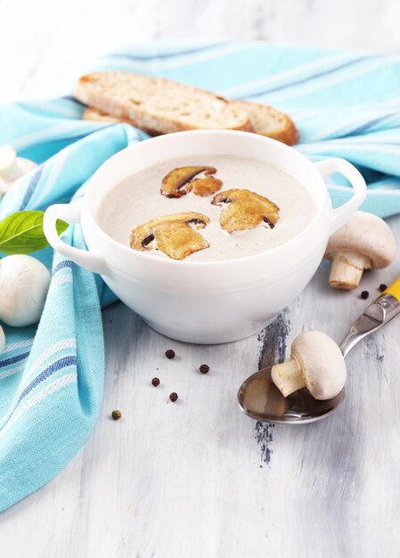 Zuppa di funghi in pentola bianca sul tovagliolo su fondo di legno