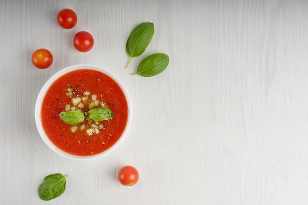 Zuppa di gazpacho rosso circondato da pomodori interi e foglie di basilico verde. Vista dall'alto