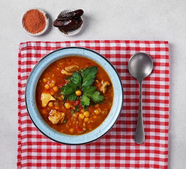 Zuppa di harira marocchina in una ciotola blu al piano del tavolo in cemento grigio e vista dall'alto del tovagliolo rosso