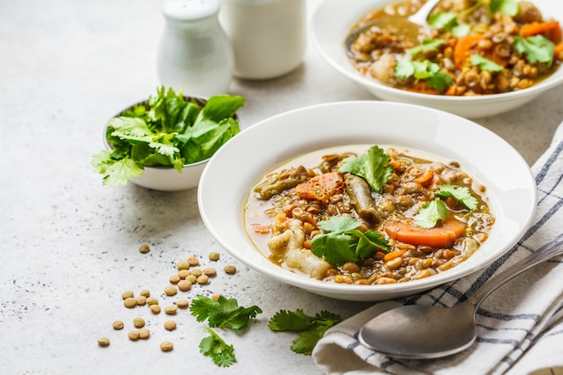 Zuppa di lenticchie con verdure in un piatto bianco, sfondo bianco, verticale. Cibo a base vegetale, mangiare pulito.