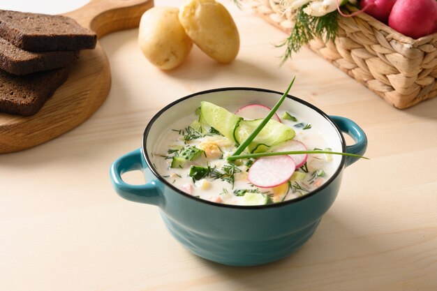 Zuppa di okroshka estiva russa fatta in casa con kefir servita con pane di segale e verdure fresche su un tavolo di legno chiaro. Avvicinamento.