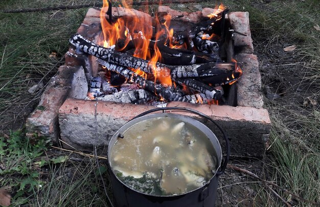 Zuppa di pesce cotta al fuoco in una casseruola vicino a una griglia accesa rivestita di mattoni