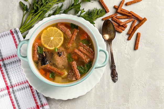 Zuppa di pesce in scatola appena preparata con una fetta di limone su uno sfondo di cemento con erbe