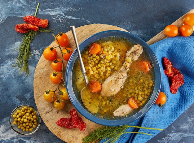 Zuppa di piselli con pollo, carote, pomodori ed erbe aromatiche in un piatto fondo su tavola di legno con tovagliolo. Disposizione piatta.