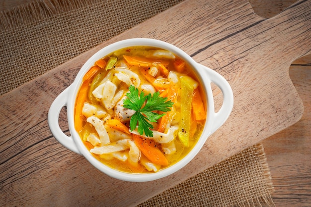 Zuppa di pollo fatta in casa russa con tagliatelle e verdure in un piatto bianco su fondo di legno