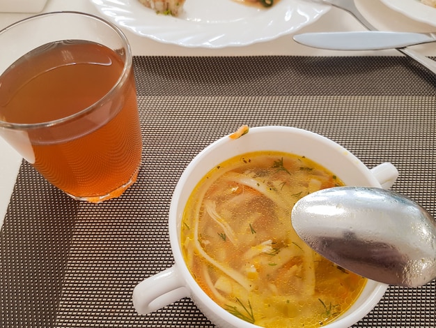 Zuppa di pollo tradizionale servita in una ciotola bianca con un cucchiaio e un bicchiere di composta, vista dall'alto, dieta sana ed equilibrata