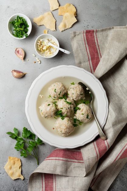 Zuppa di polpette di pollo matzo fatta in casa con prezzemolo e aglio in un semplice piatto di ceramica bianca su una pietra grigia o cemento