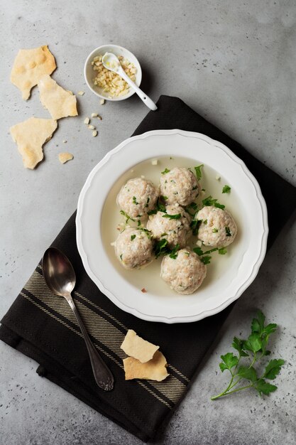 Zuppa di polpette di pollo matzo fatta in casa con prezzemolo e aglio in un semplice piatto di ceramica bianca su una pietra grigia o cemento