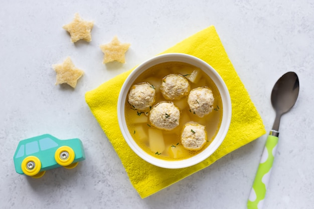 Zuppa di polpette per bambini con crostini con macchinina, cucchiaio e tovaglia gialla