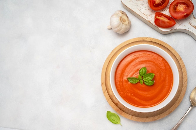 Zuppa di pomodoro con basilico fresco in una ciotola arancione Sfondo luminoso Concetto di cibo sano Copia spazio