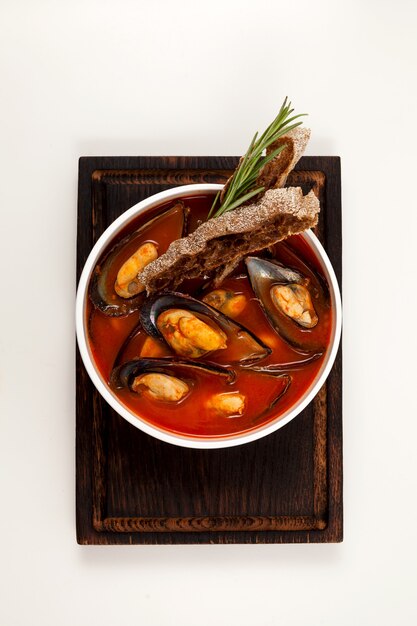 Zuppa di pomodoro con cozze in un piatto fondo bianco sul tagliere di legno scuro.