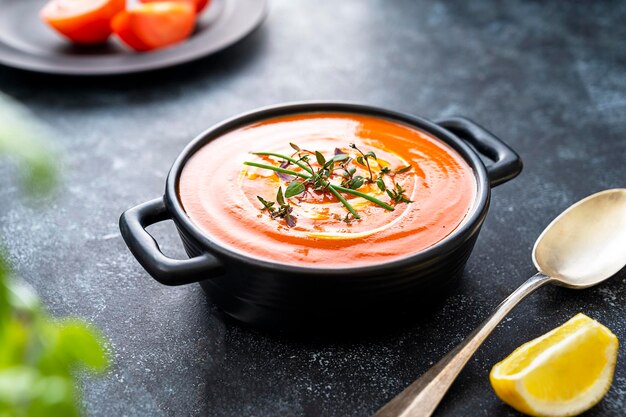 Zuppa di pomodoro con erbe fresche in ciotola nera Sfondo scuro Zuppa cremosa vegana