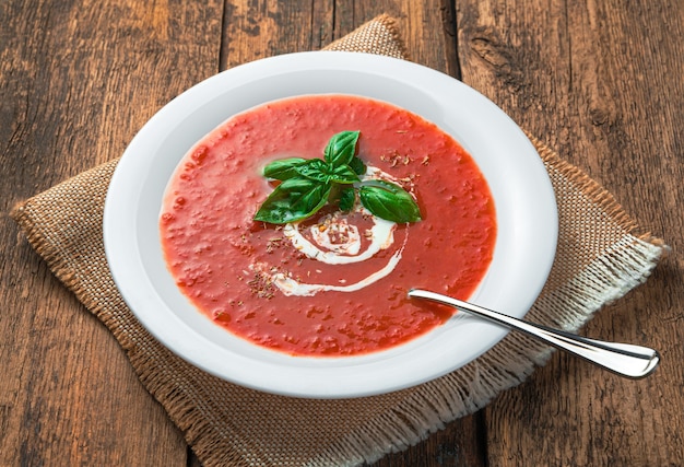 Zuppa di pomodoro con panna e basilico fresco su fondo di legno