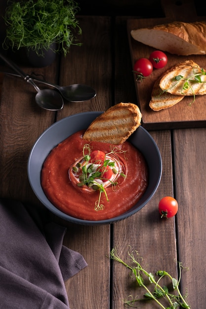 Zuppa di pomodoro fatta in casa in una ciotola blu con pane tostato su un tavolo di legno