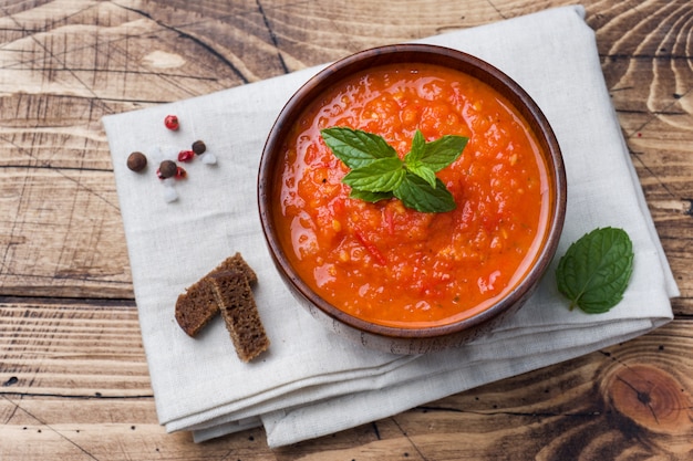 Zuppa di pomodoro in una ciotola di legno con pezzi di pane tostato su un tavolo rustico.