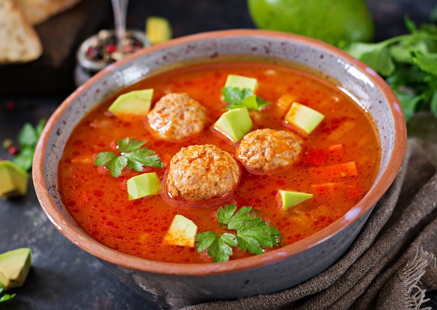 Zuppa di pomodoro piccante con polpette e verdure. Servito con avocado e prezzemolo.