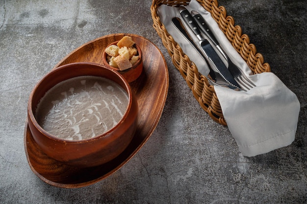 Zuppa di purè di funghi in una ciotola di legno su un vassoio con briciole di pane contro un tavolo di pietra grigia