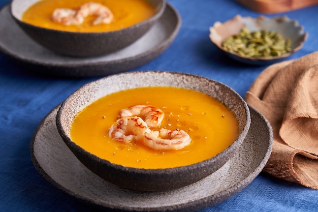 Zuppa di purea di crema di zucca e carote sana vegetariana con gamberetti e spezie a prua sulla tovaglia