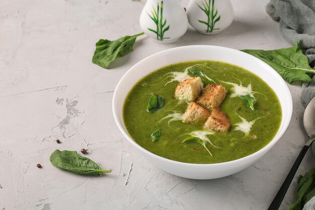 Zuppa di purea di spinaci verdi servita con crostini in una ciotola bianca su sfondo grigio chiaro, primo piano