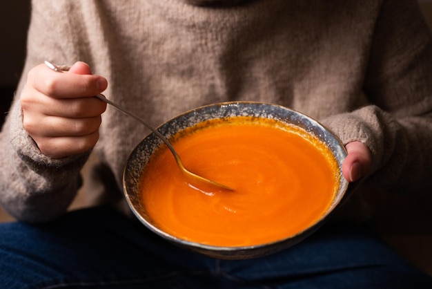Zuppa di purea di verdure, mano femminile che raccoglie zuppa di crema di zucca da un piatto con un cucchiaio.