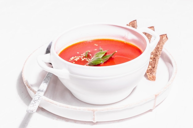 Zuppa di purea rossa con pomodoro, verdure e pane. Luce dura alla moda, ombra scura. Sfondo bianco stucco, primo piano