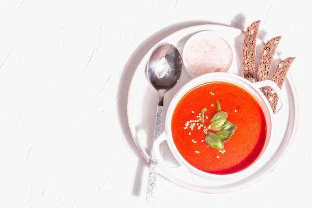 Zuppa di purea rossa con pomodoro, verdure e pane. Luce dura alla moda, ombra scura. Sfondo bianco stucco, vista dall'alto