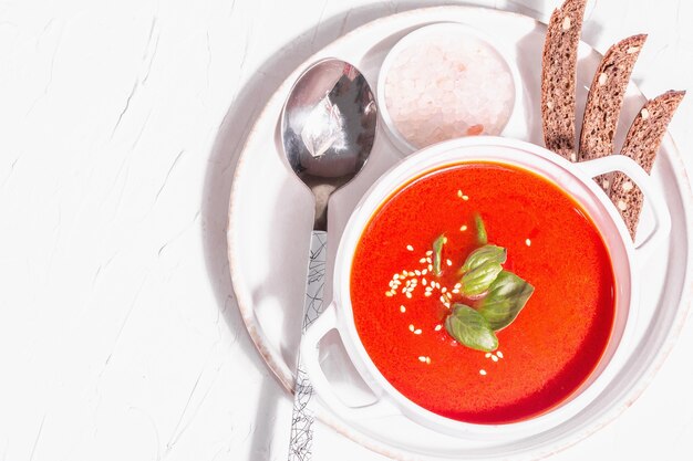 Zuppa di purea rossa con pomodoro, verdure e pane. Luce dura alla moda, ombra scura. Sfondo bianco stucco, vista dall'alto