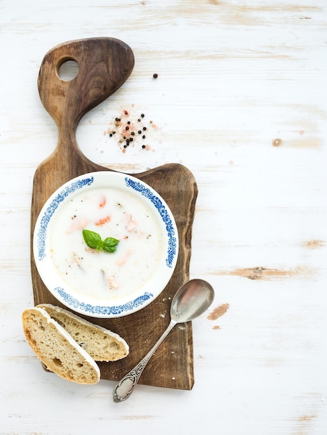 Zuppa di salmone scandinavo con crema di basilico fresco e pane in piatto di ceramica vintage su tavola da portata in legno su sfondo bianco vista dall'alto