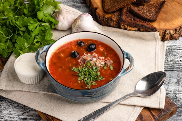 Zuppa di Solyanka Solyanka con panna acida su fondo bianco di legno