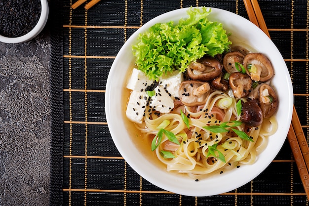 Zuppa di spaghetti vegana con formaggio tofu, funghi shiitake e lattuga in una ciotola bianca.