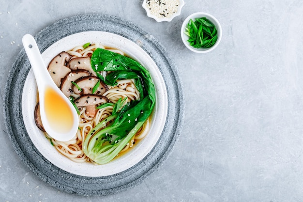 Zuppa di spaghetti vegetariani asiatici Udon o Ramen in una ciotola con funghi Shiitake e Bok Choy su sfondo di pietra grigia Vista dall'alto spazio di copia