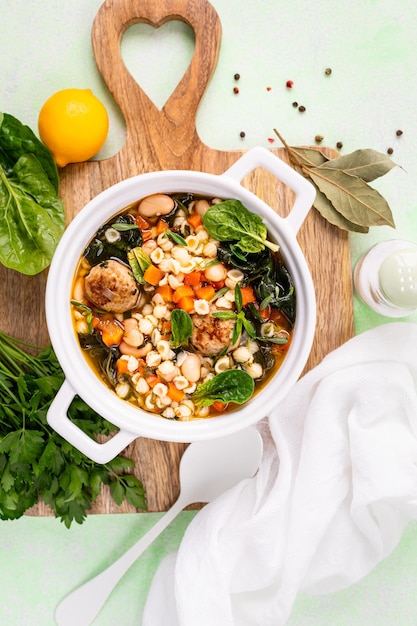 Zuppa di verdure casalinga con polpette e spinaci in una padella bianca su uno sfondo verde