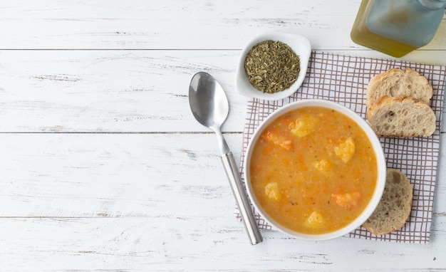 Zuppa di verdure in una ciotola con condimenti e fette di pane su un tavolo di legno con spazio per la copia