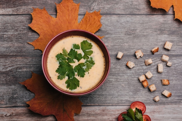 Zuppa di verdure vegetariana crema di zucca con prezzemolo in una ciotola su un tavolo di legno con pomodori e cracker.