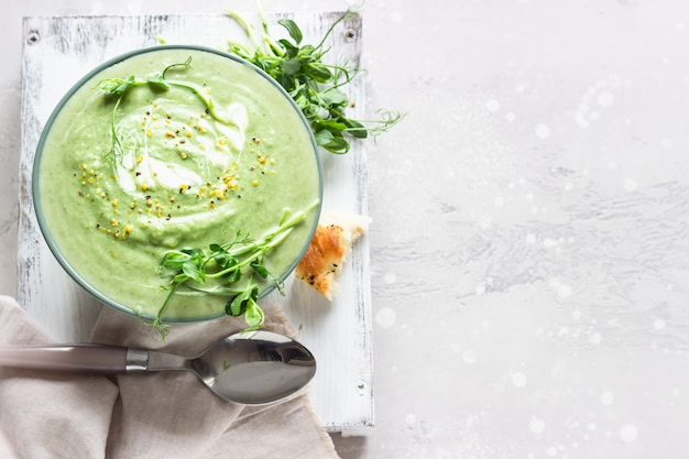 Zuppa di verdure verdi di primavera in una ciotola servita con micro verdure, panna e focaccia fresca
