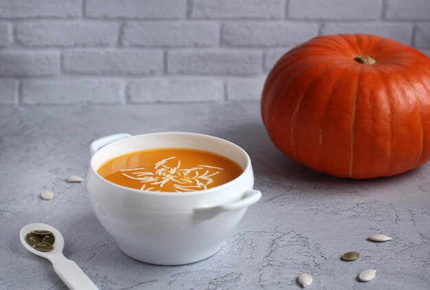 Zuppa di zucca con salsa e semi di zucca in una tazza bianca su sfondo grigio