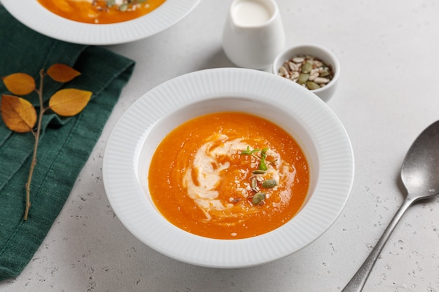 zuppa di zucca con semi e panna in un piatto bianco su un tavolo grigio