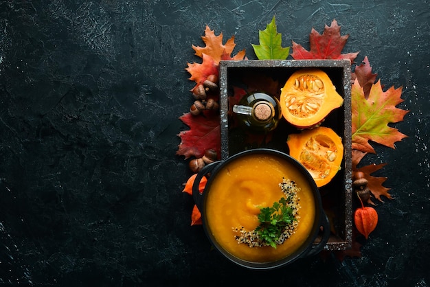 Zuppa di zucca con zucca e foglie autunnali colorate distese su uno sfondo di pietra nera Vista dall'alto Spazio libero per il testo