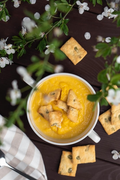 Zuppa di zucca cremosa organica speziata fresca in una ciotola bianca sul tavolo di legno con cracker di pane