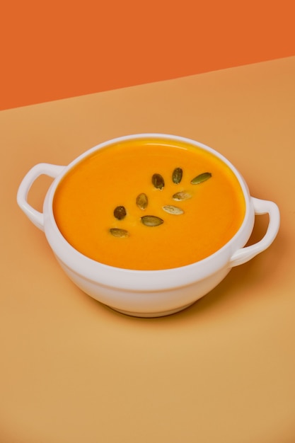 Zuppa di zucca decorata con semi di zucca isolati su sfondo arancione. Monocromatico, minimalismo. Vista dall'alto. Copia spazio.