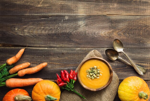 Zuppa di zucca fresca fatta in casa con ingredienti su fondo rustico in legno. Vista dall'alto. Copia spazio.