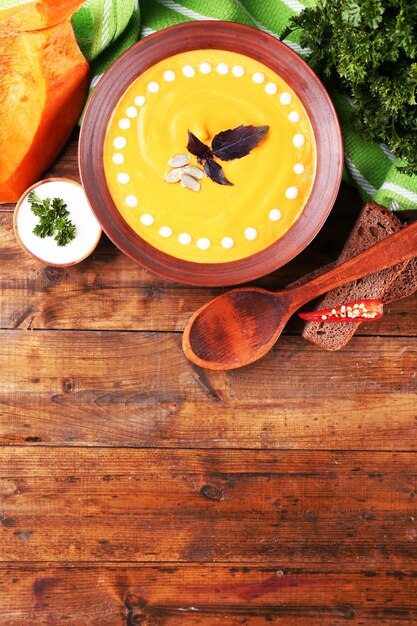 Zuppa di zucca in piatto di colore e fetta di zucca sul tovagliolo su fondo di legno