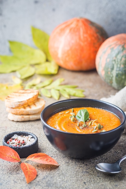 Zuppa di zucca in un piatto nero su una pietra. Decorazioni autunnali.