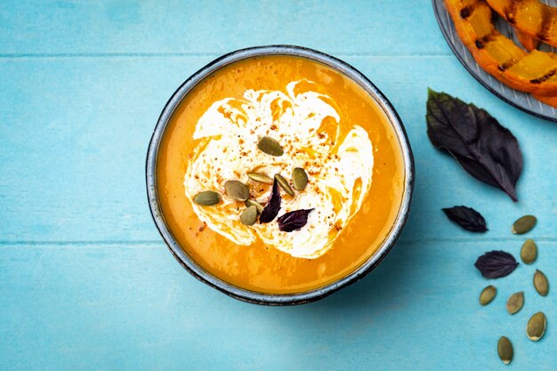 Zuppa di zucca in un piatto su una superficie di legno blu.