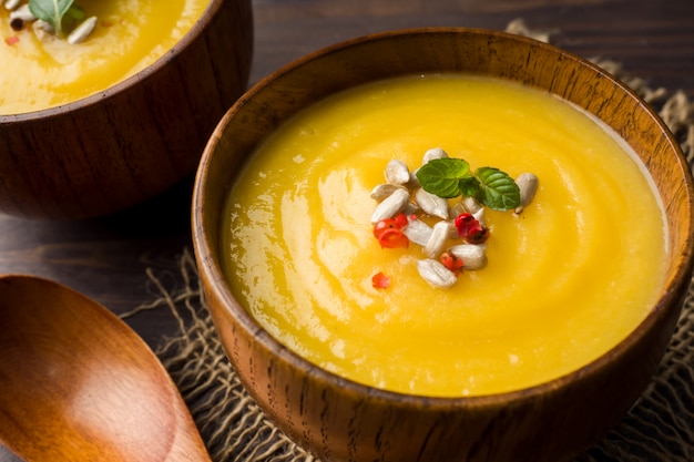 Zuppa di zucca schiacciata con spezie in ciotole di legno su tavole scure.