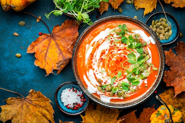 Zuppa di zucca vegana con semi crema di cocco e germogli di piselli verdi Inverno o autunno sano vegetariano slow food Ciotola di zuppa su sfondo blu tavolo Vista dall'alto