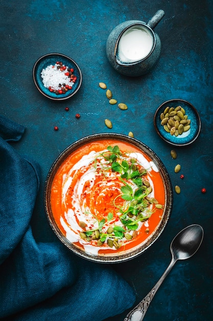 Zuppa di zucca vegana con semi crema di cocco e germogli di piselli verdi Inverno sano vegetariano slow food Ciotola di zuppa su sfondo blu tavolo Vista dall'alto