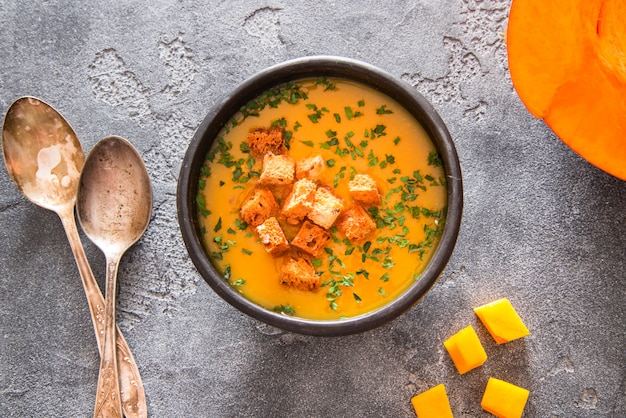 Zuppa di zucca vegana in ciotola di ceramica nera su superficie scura, vista dall'alto